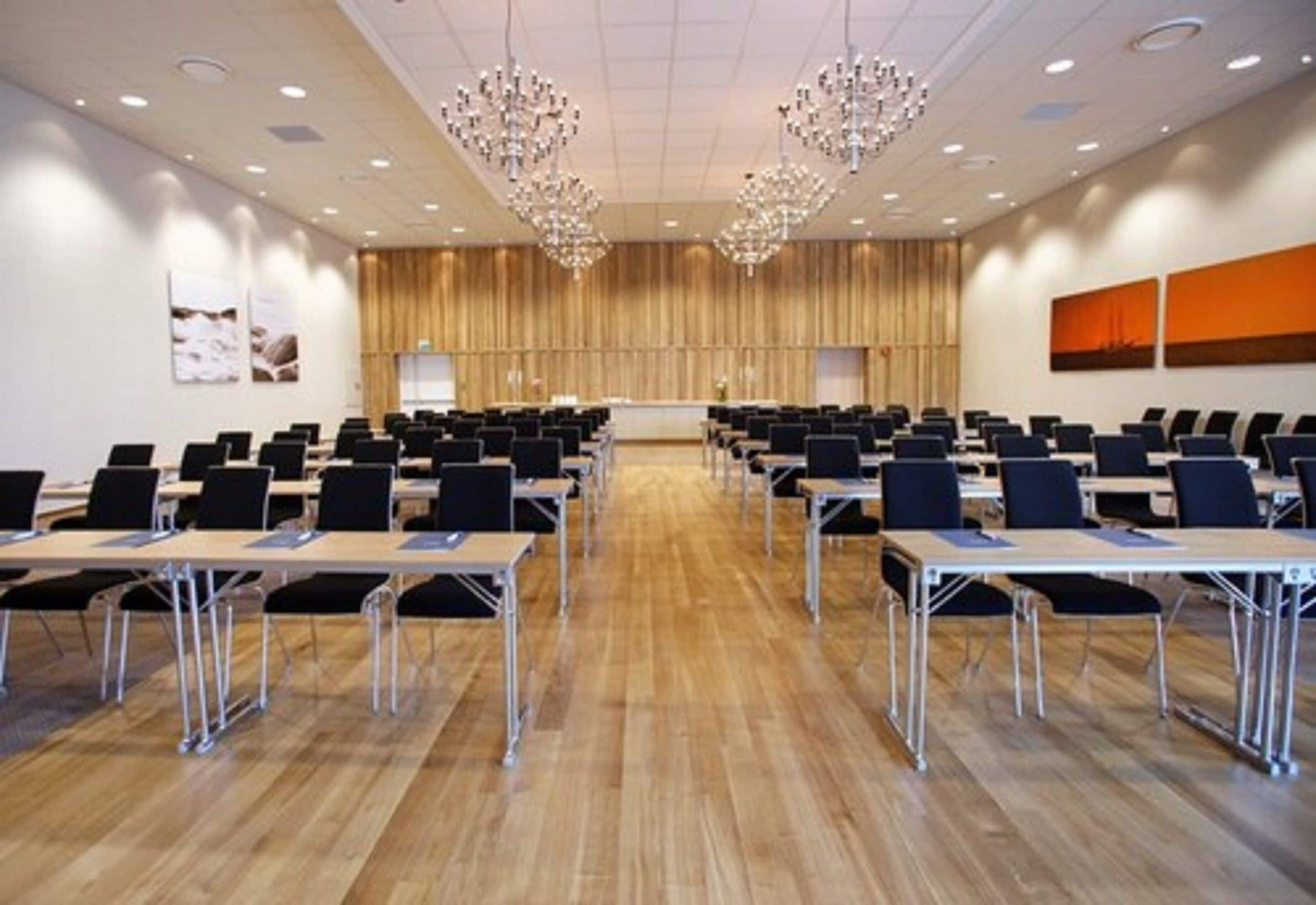 Ein Konferenzraum mit Tischen und Stühlen, Holzwandverkleidung und Kronleuchtern.