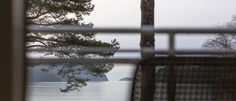 A view through a window with a metal grid, overlooking a calm lake with distant islands and a bench in the foreground.