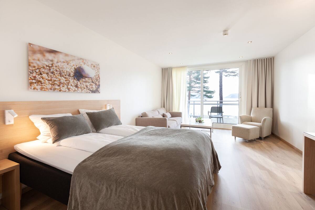 Ein modernes Hotelzimmer mit einem großen Bett, einer Couch, einem Sessel und einem Balkon mit Blick.