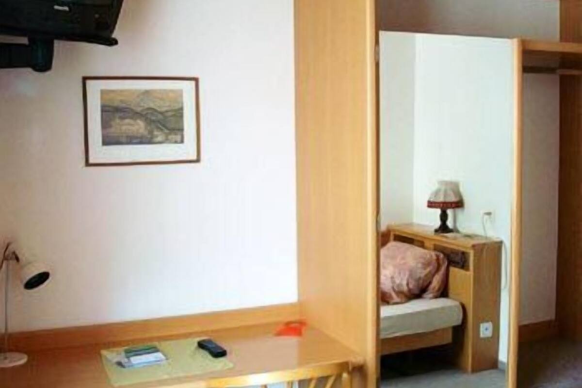 A compact room with a bed, a desk, a lamp, and a television.