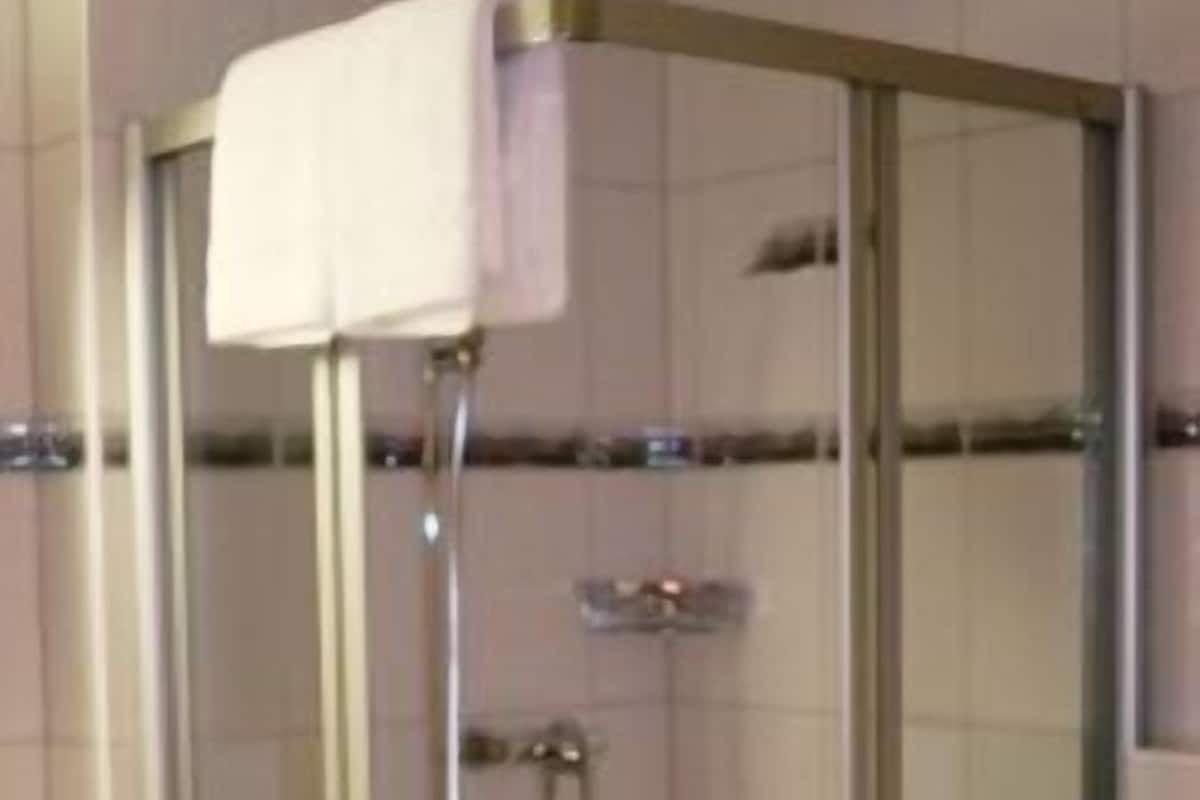 A glass-enclosed shower stall with a handheld showerhead and a towel rack above.