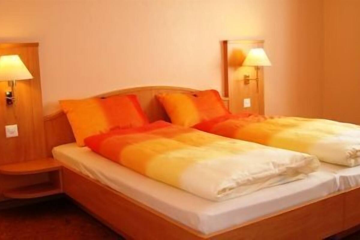 A double bed with orange and white bedding, two bedside tables with lamps, and a wooden headboard.