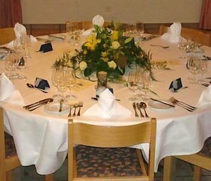 Una mesa redonda para comer dispuesta con manteles blancos, cristalería y un centro de mesa con flores amarillas.