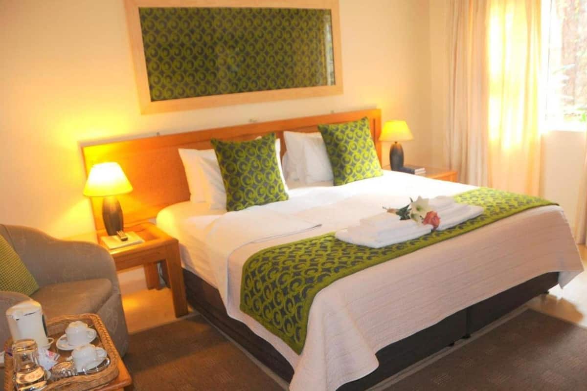 Une chambre d’hôtel comprenant un lit, deux tables de chevet avec des lampes, une chaise et une petite table sur laquelle se trouve un plateau avec divers objets.