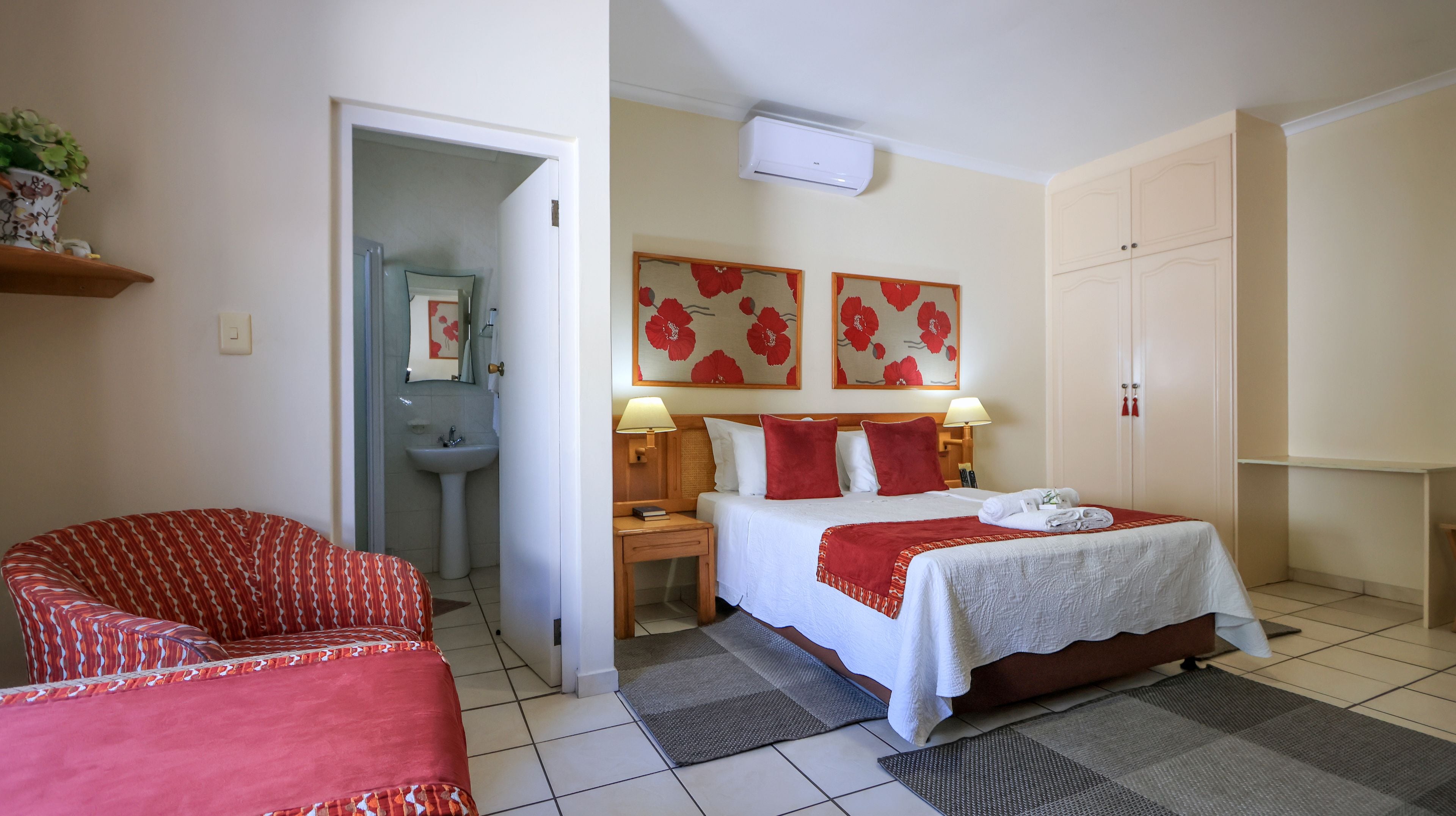 Ett hotellrum med en säng, sänglampor, ett badrum, en garderob och en röd stol med mönster.