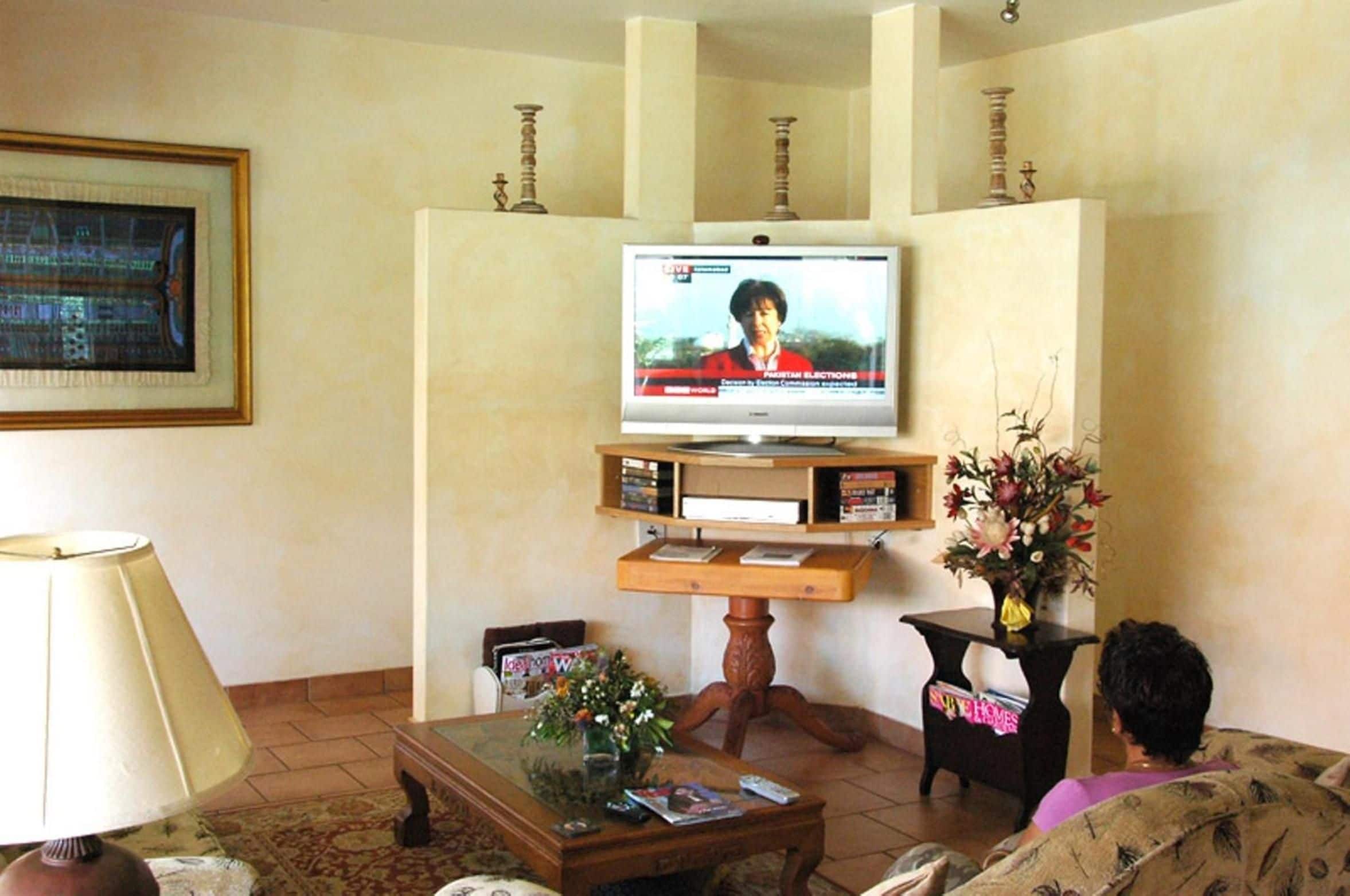 A living room with a television mounted on a wall, a coffee table with magazines, a lamp, and a floral arrangement.
