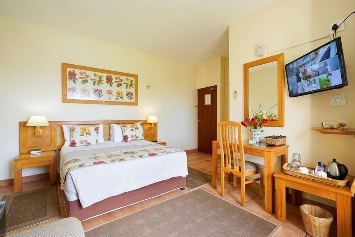 Une chambre d’hôtel comprenant un lit, des lampes de chevet, un bureau avec une chaise, une télévision, un miroir et un tableau représentant des fleurs accroché au mur.
