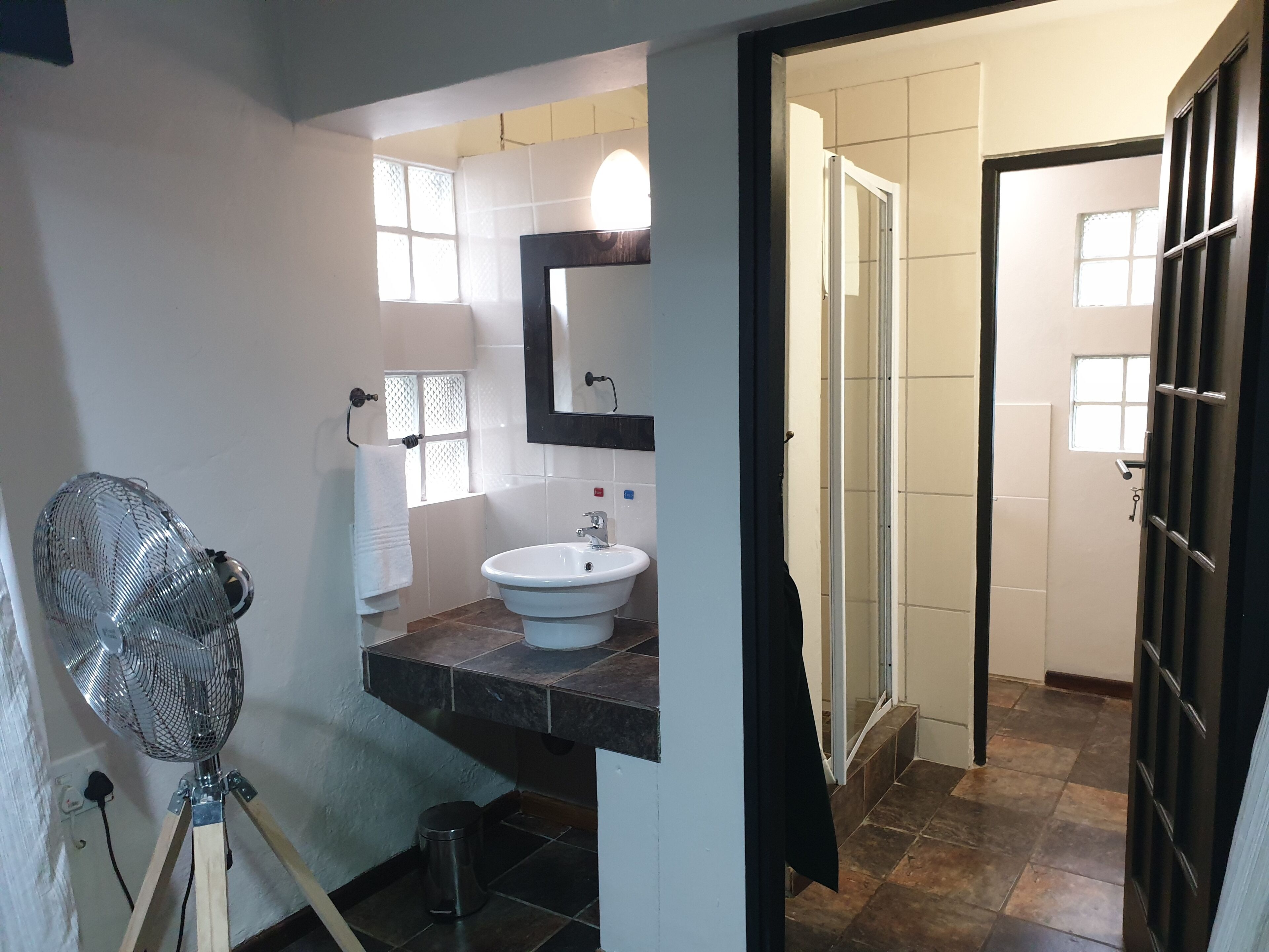 Een badkamer met een wastafel, spiegel en ventilator.