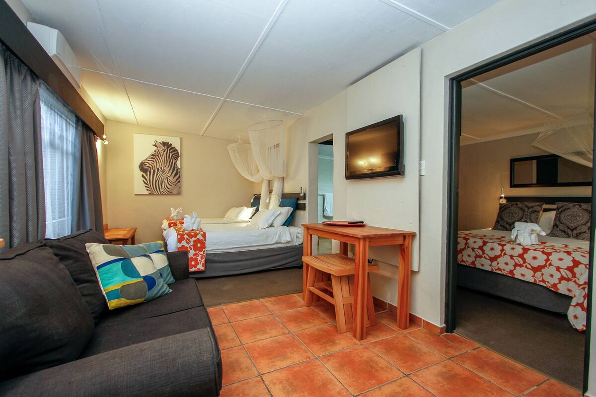 A hotel room with a bed, a sofa, a small wooden table, a TV, and a large mirror.