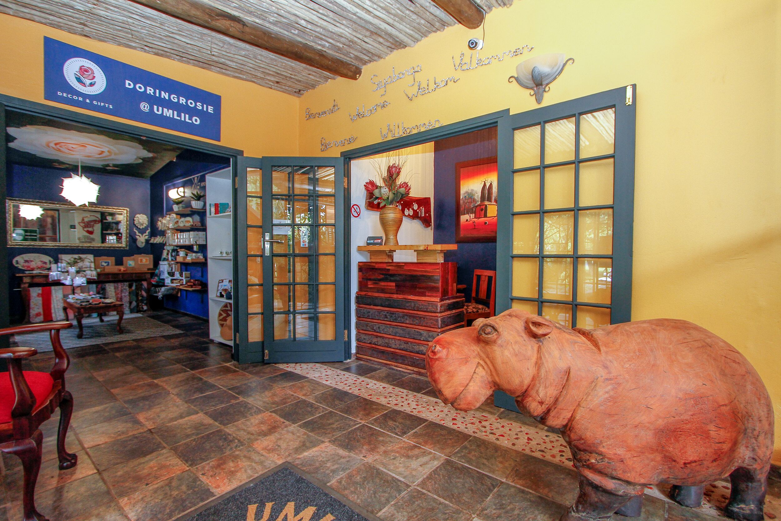 Un hall d’hôtel avec une grande sculpture d’éléphant en bois, un comptoir d’accueil et une enseigne bleue portant le nom « Doringrosie ».