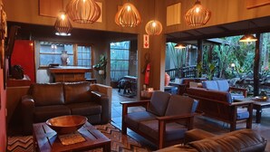 A spacious living area with leather sofas, wooden coffee tables, and pendant lighting. A large window offers a view of the outdoors. - Umlilo Lodge (St. Lucia)