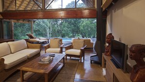 A spacious living area with a high ceiling, wooden furniture, and a large window offering a view of the outdoors.