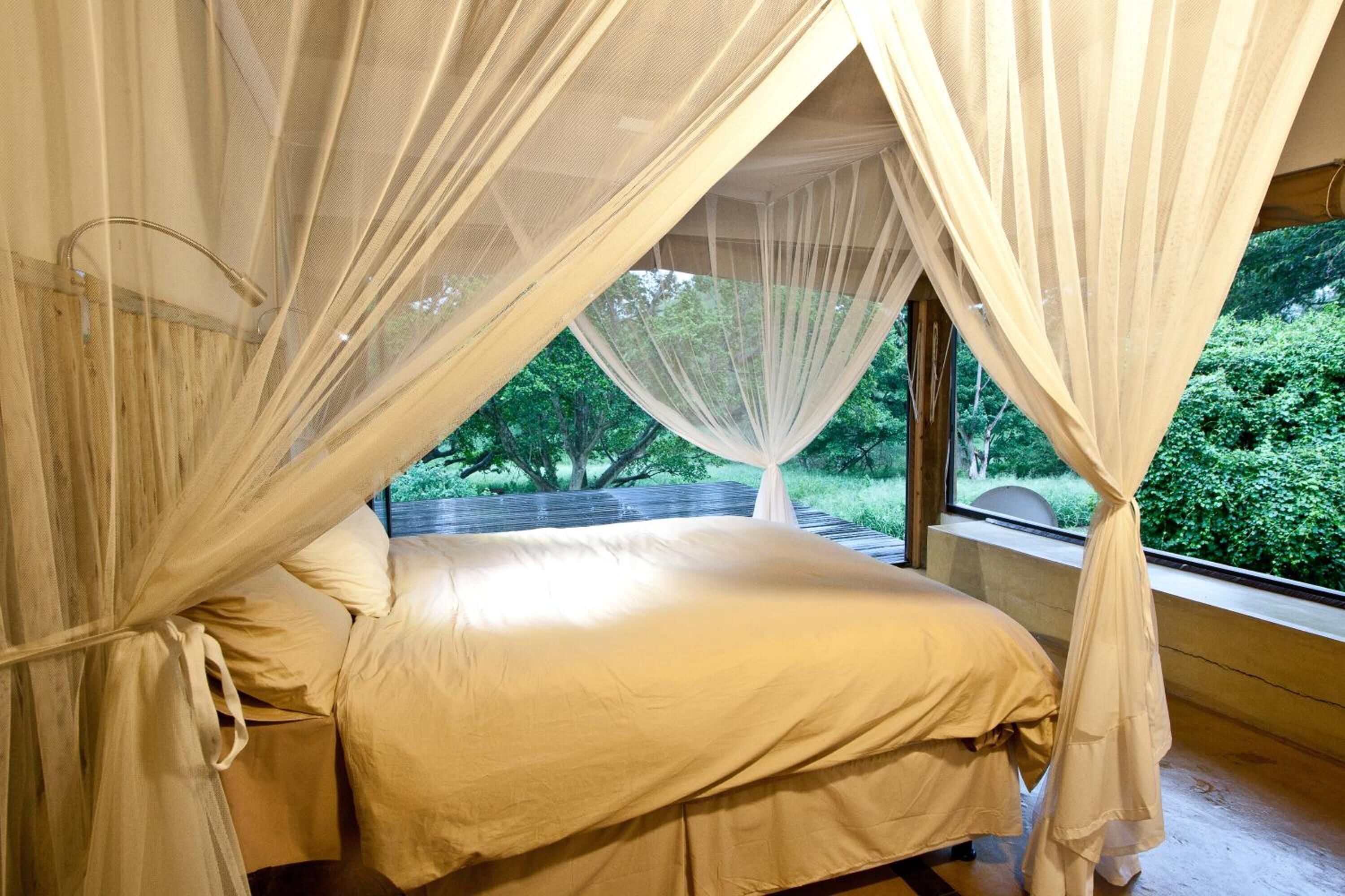 Una cama con dosel, una ventana y vistas al verdor exterior.