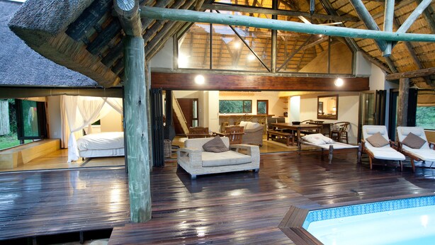 A spacious indoor area with a wooden deck, a pool, and a dining area with multiple chairs and tables.
