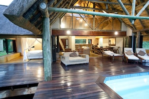 Amplio espacio interior con una terraza de madera, piscina y zona de comedor con múltiples sillas y mesas.