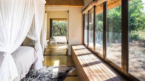 A bedroom with a canopy bed, a view of a forest, and a large window.