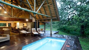 A wooden deck with a pool, lounge chairs, and a dining area with tables and chairs.