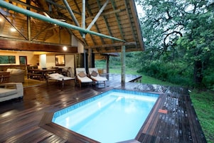 Una terraza de madera con piscina, sillas de descanso y un área de comedor con mesas y sillas.