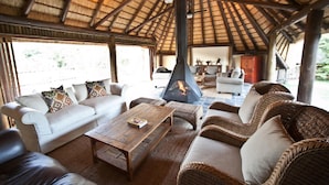 A cozy lounge area with a thatched roof, wicker furniture, and a central fire feature.