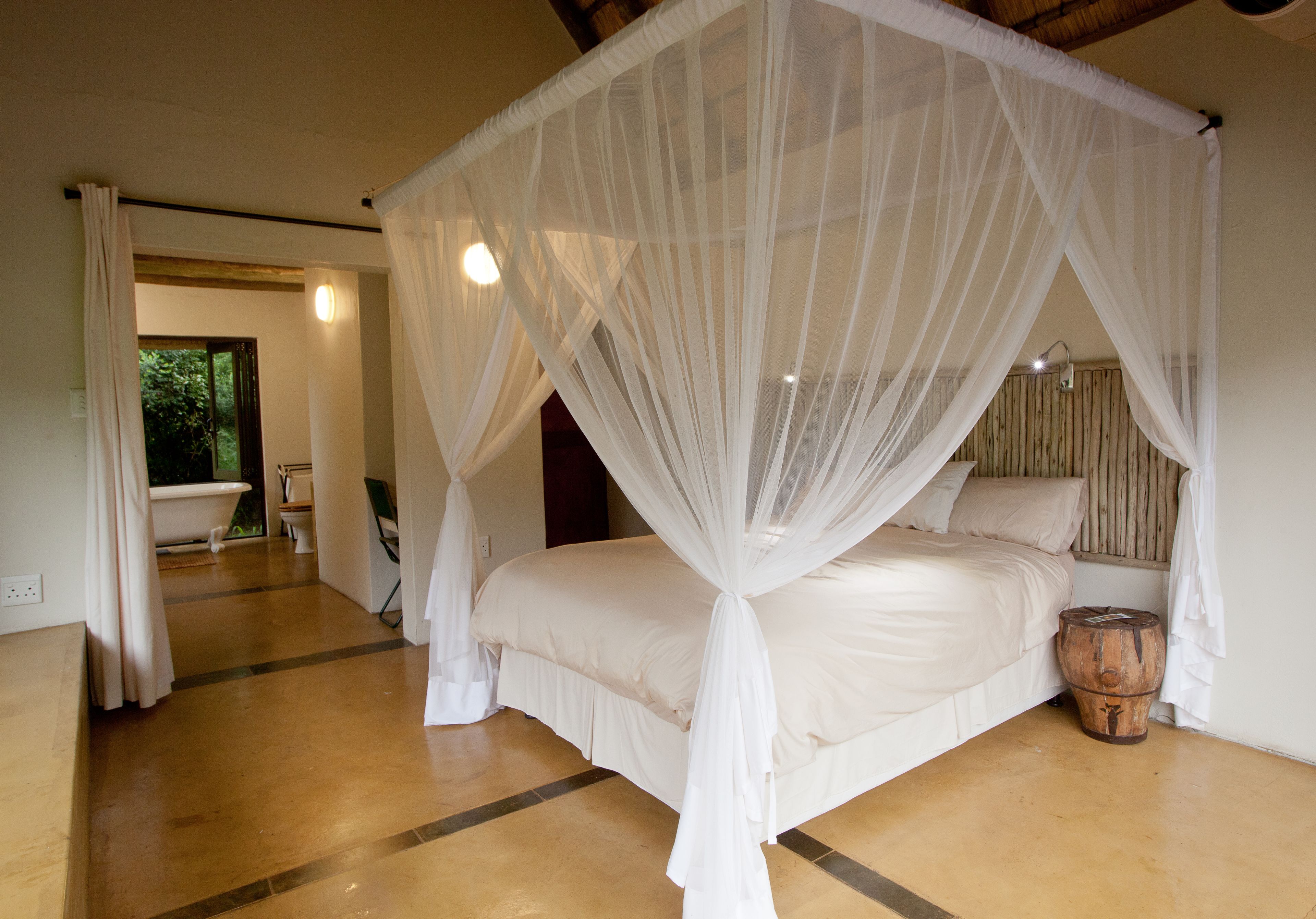 Un dormitorio con cama con dosel, un barril de madera y vista al baño.