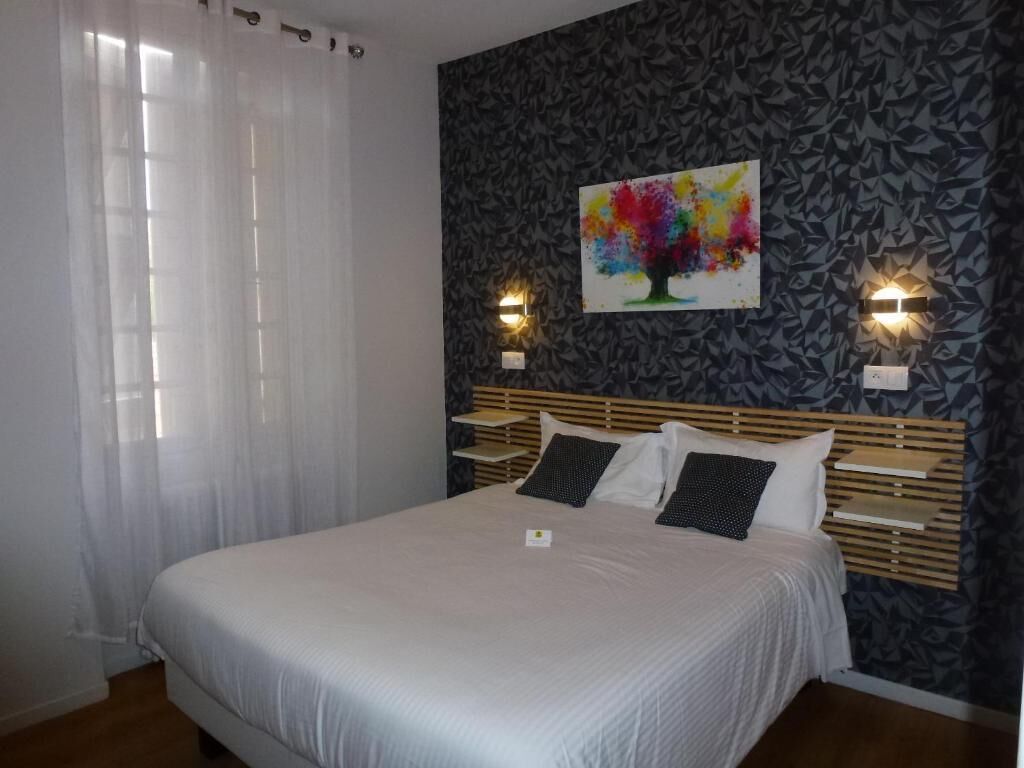 A bedroom with a bed, two bedside lamps, a wall with a colorful abstract painting, and a window with sheer curtains.