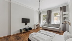 A modern hotel room with a large bed, a TV mounted on the wall, a sofa, and a desk with a chair. - Pension 1A Apartment (Berlin)
