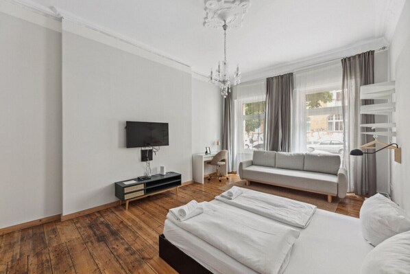 A modern hotel room with a large bed, a TV mounted on the wall, a sofa, and a desk with a chair. - Pension 1A Apartment (Berlin)
