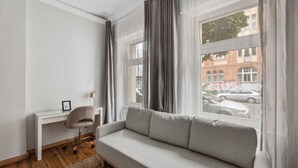 A modern living room with a grey sofa, a small desk, and a chair. - Pension 1A Apartment (Berlin)