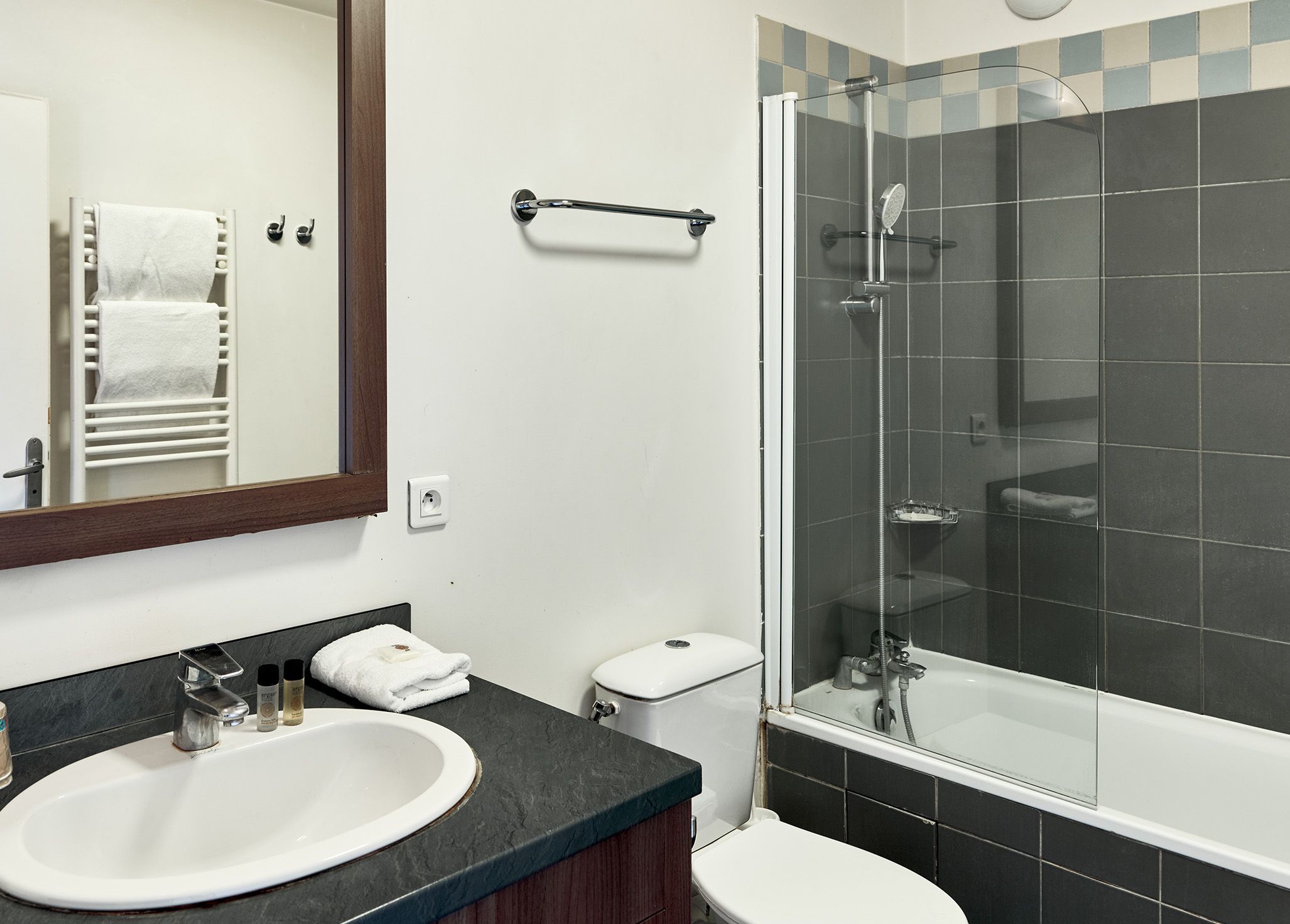 Une salle de bain moderne avec un lavabo blanc, un plan de toilette foncé et une douche à parois de verre.
