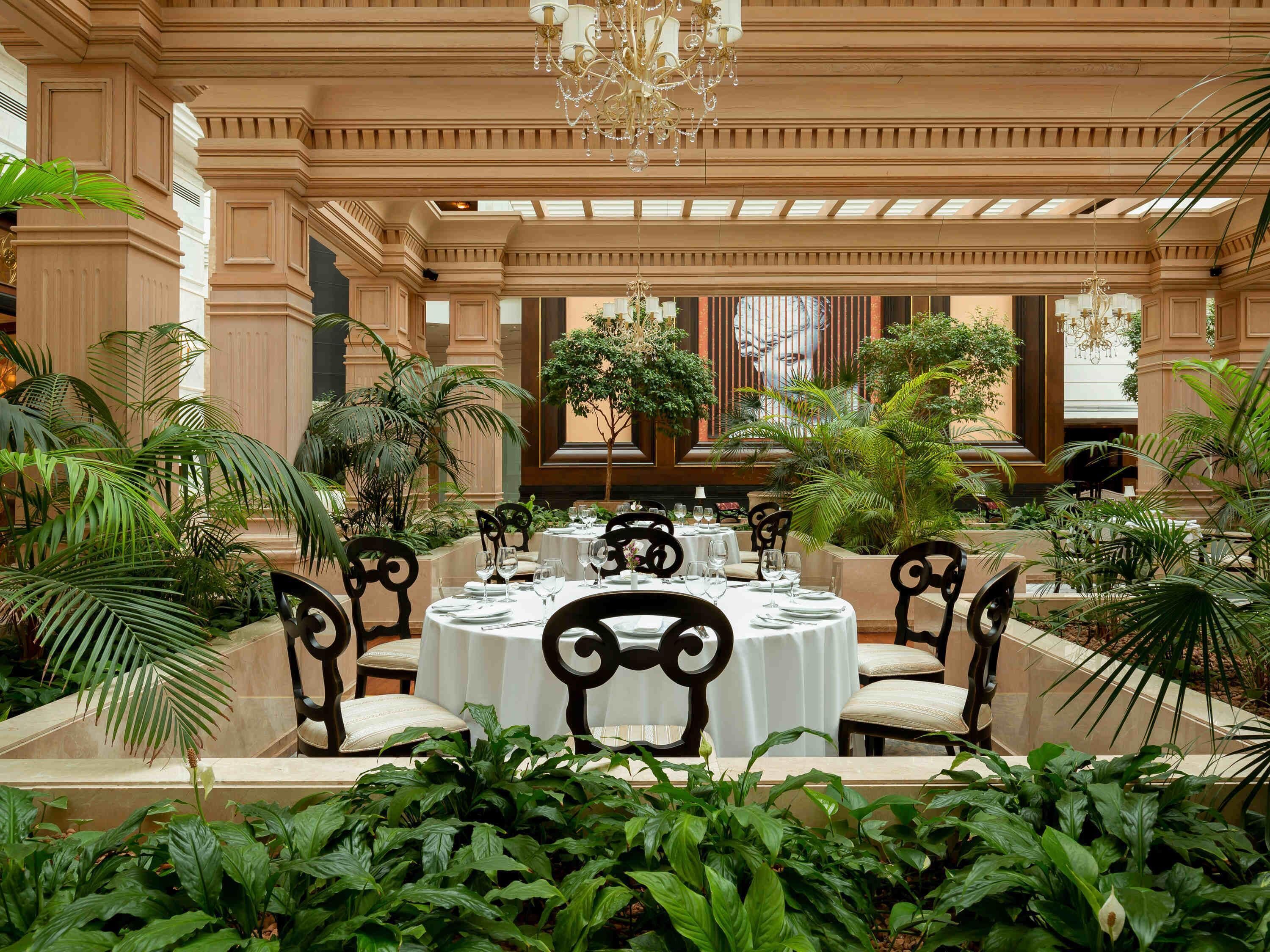Un espace de restauration intérieur luxueux, avec des tables rondes, des chaises élégantes et une végétation luxuriante.