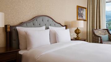 A hotel room with a large bed, a nightstand, a lamp, a chair, and a painting on the wall.