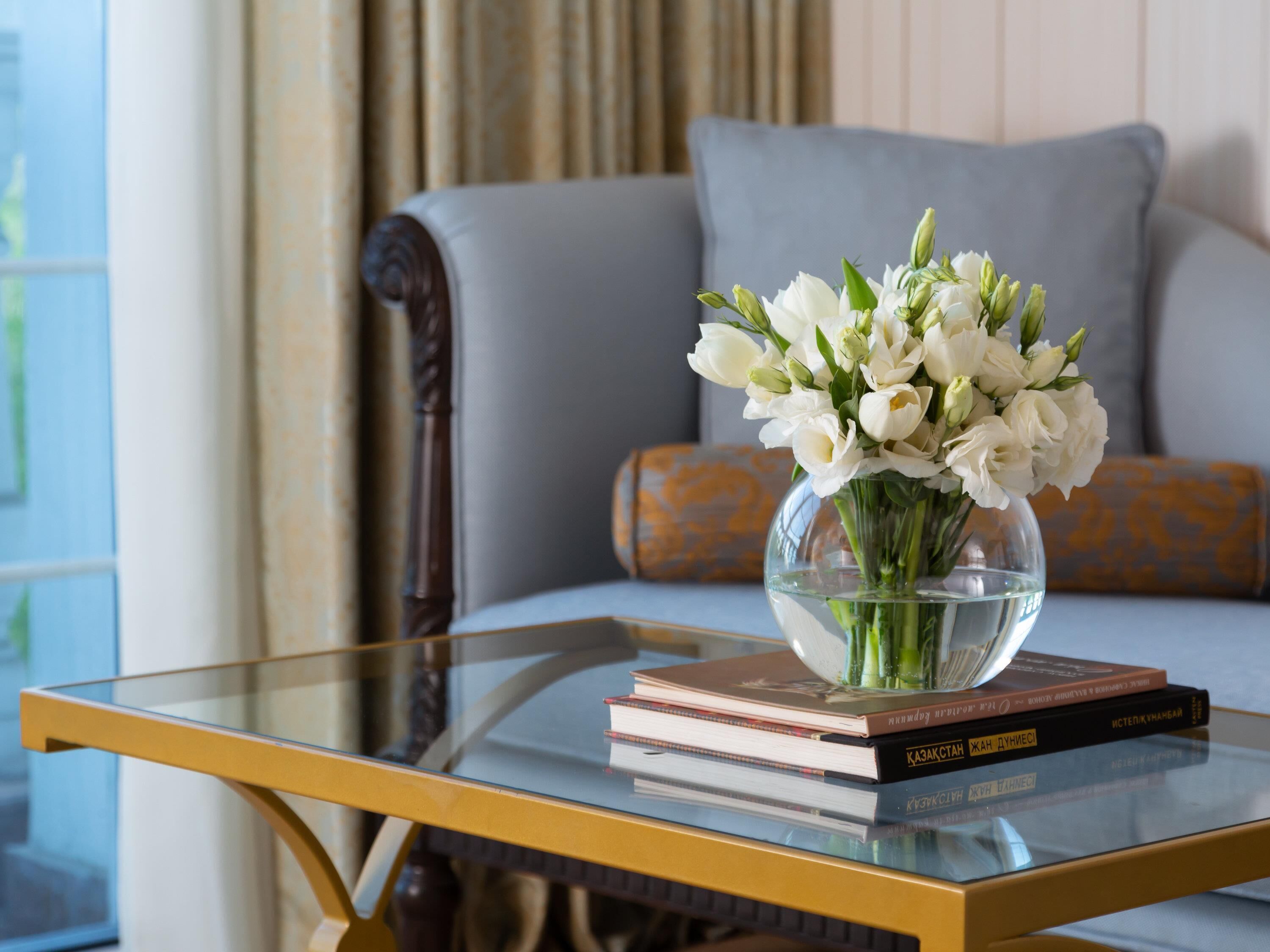 A glass coffee table with a vase of white flowers and books.
