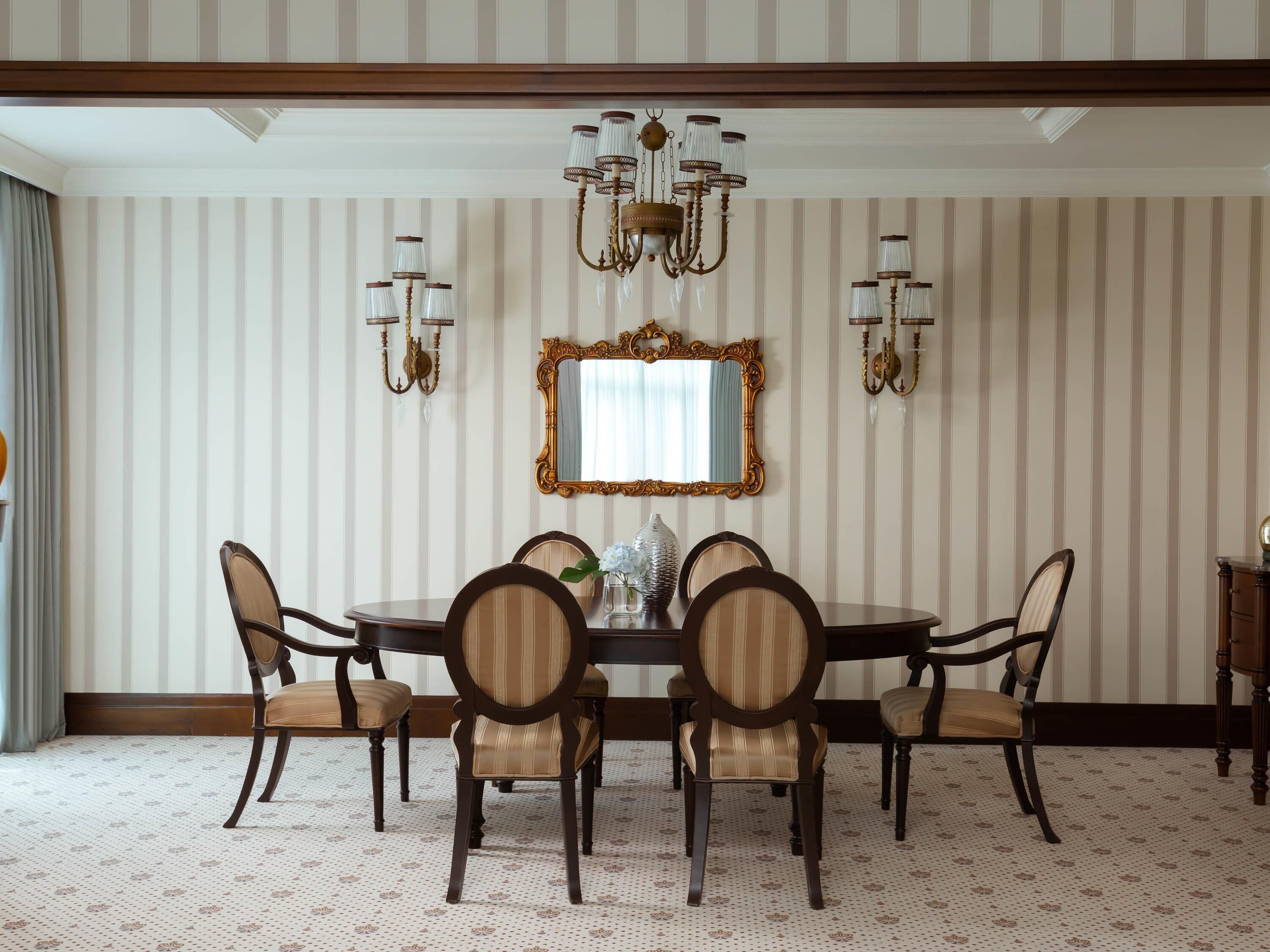 A dining room with a round table, six chairs, a chandelier, wall sconces, and a mirror.