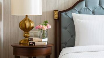 A neatly made bed with a tufted headboard, a bedside table with a lamp, books, and a vase of flowers.