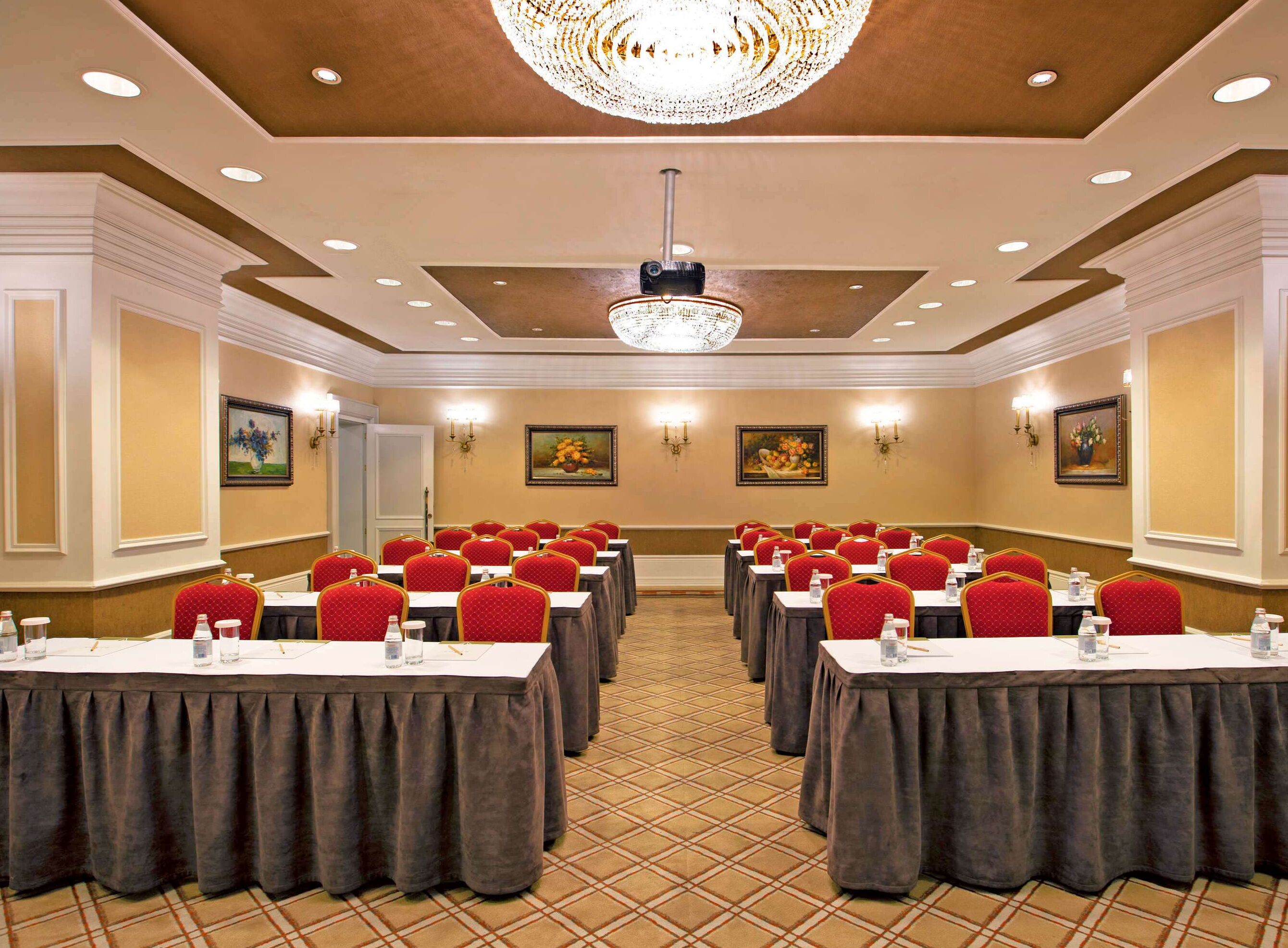 Un salón de conferencias con varias mesas y sillas, un candelabro e iluminación en las paredes.