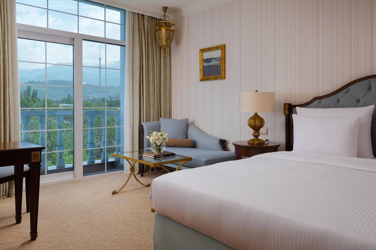 A hotel room with a large bed, a sofa, a desk, and a view of mountains through the window.