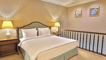 Una camera d'albergo con un letto grande, due comodini con lampade, un tavolino e una ringhiera decorativa.