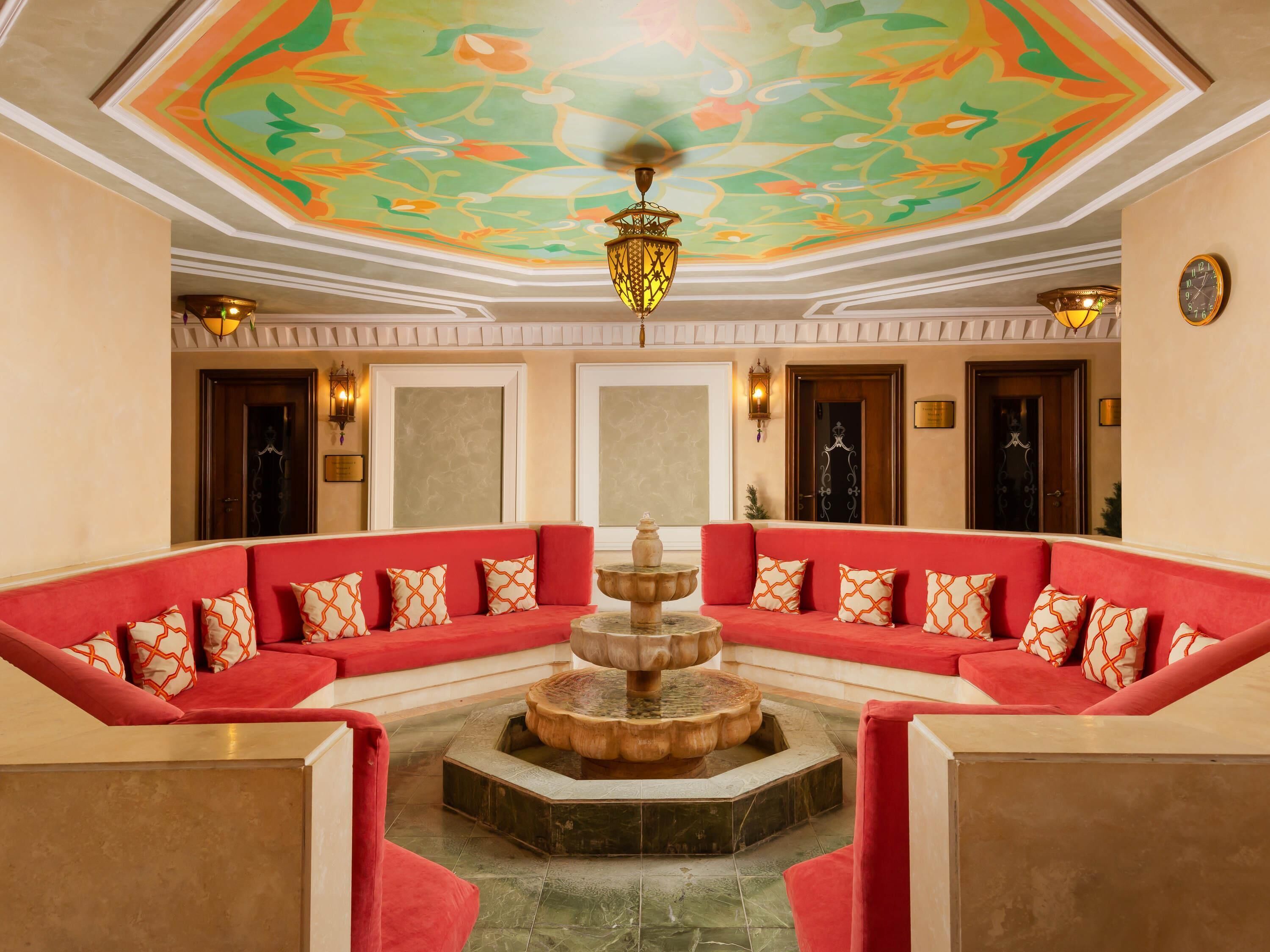 A lobby with a central fountain, red sofas with patterned cushions, and a decorative ceiling.