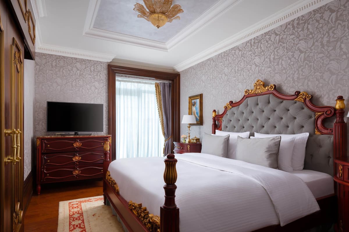 A spacious bedroom with a large bed, a dresser, a television, and a chandelier.