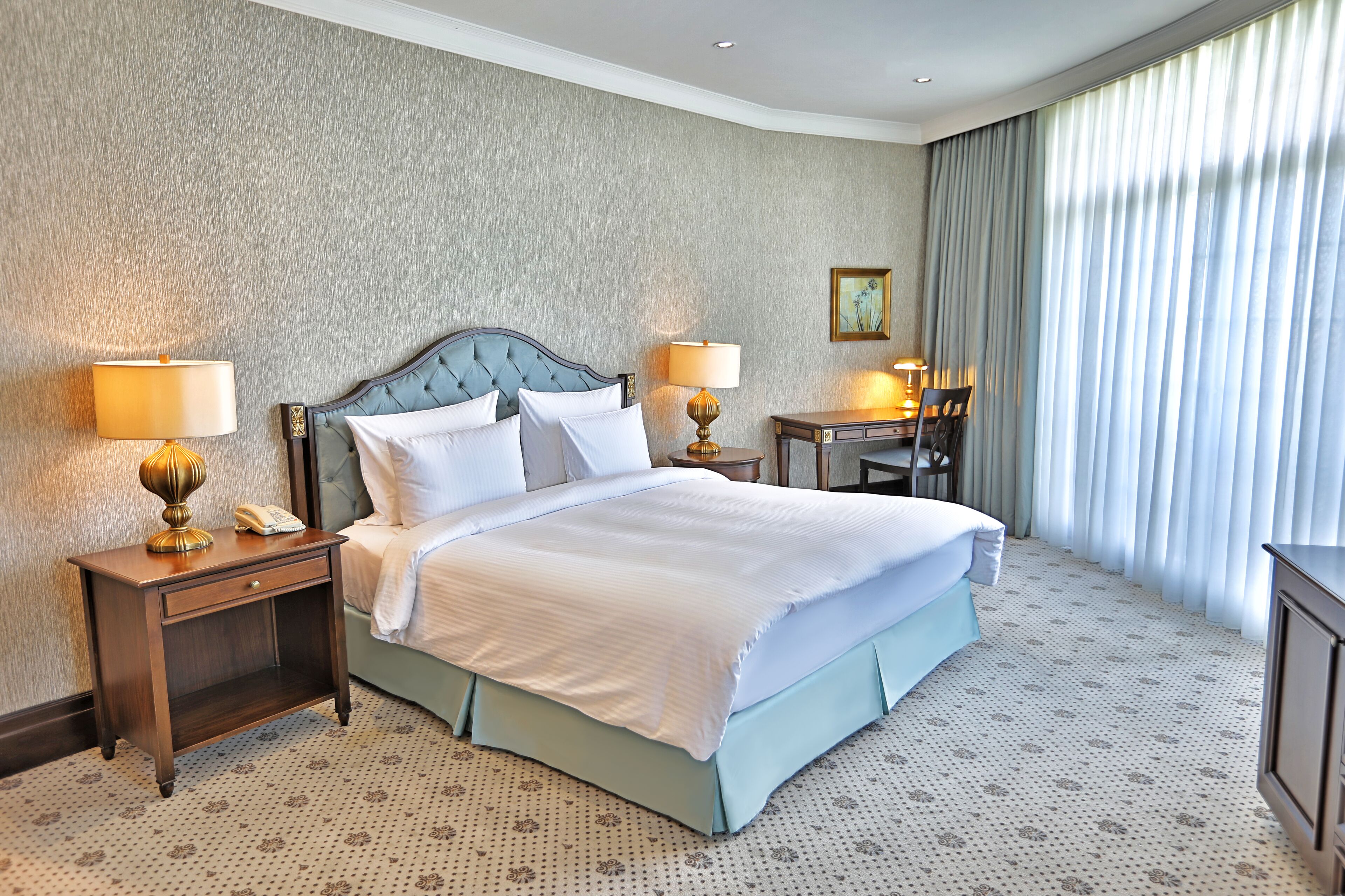 A hotel room with a large bed, two bedside tables with lamps, a small desk, and a chair.