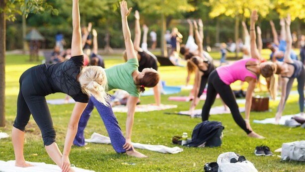 A group of people performing yoga in an outdoor setting with grass and trees.