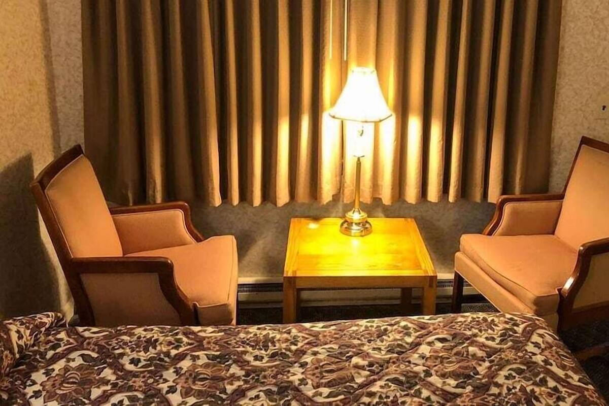 Ein Hotelzimmer mit einem Bett, zwei Sesseln, einem kleinen Tisch, einer Lampe und einem Vorhang im Hintergrund.