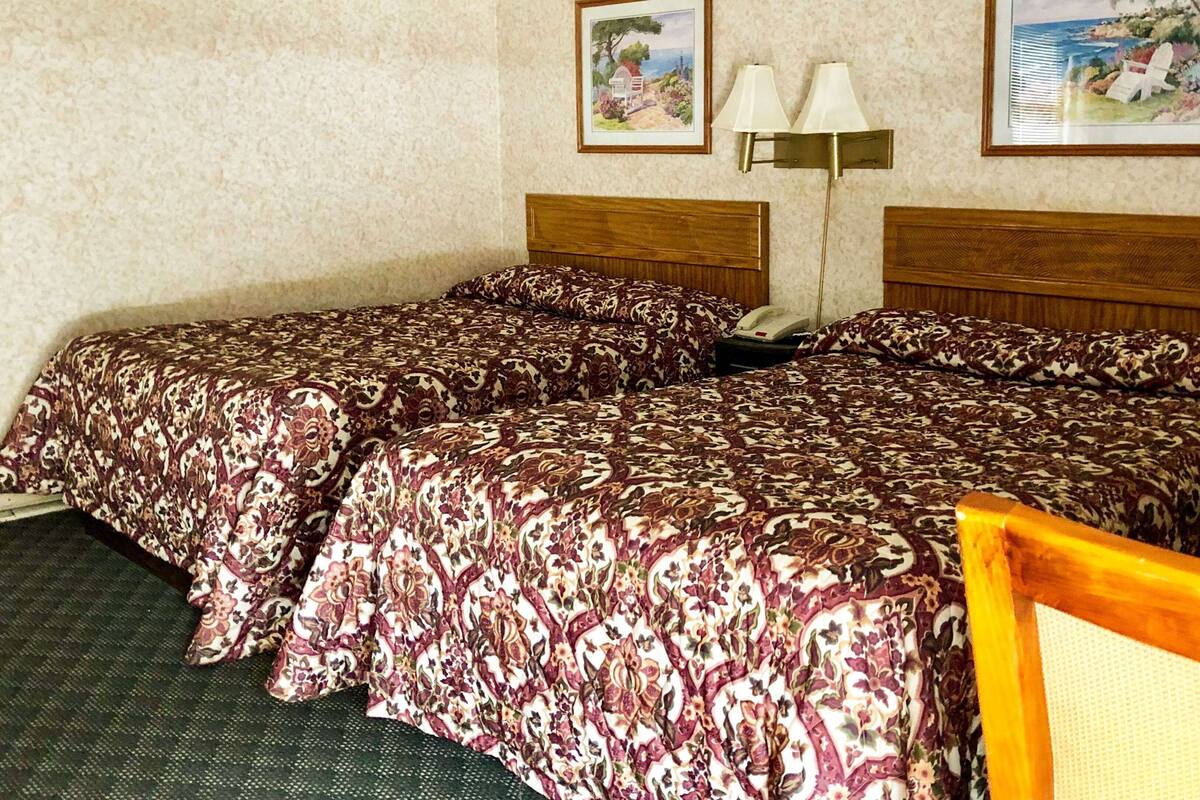 Ein Hotelzimmer mit zwei Betten, einem Nachttisch mit Lampe und zwei gerahmten Bildern an der Wand.