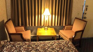 A hotel room with a bed, two chairs, a small table, and a lamp.