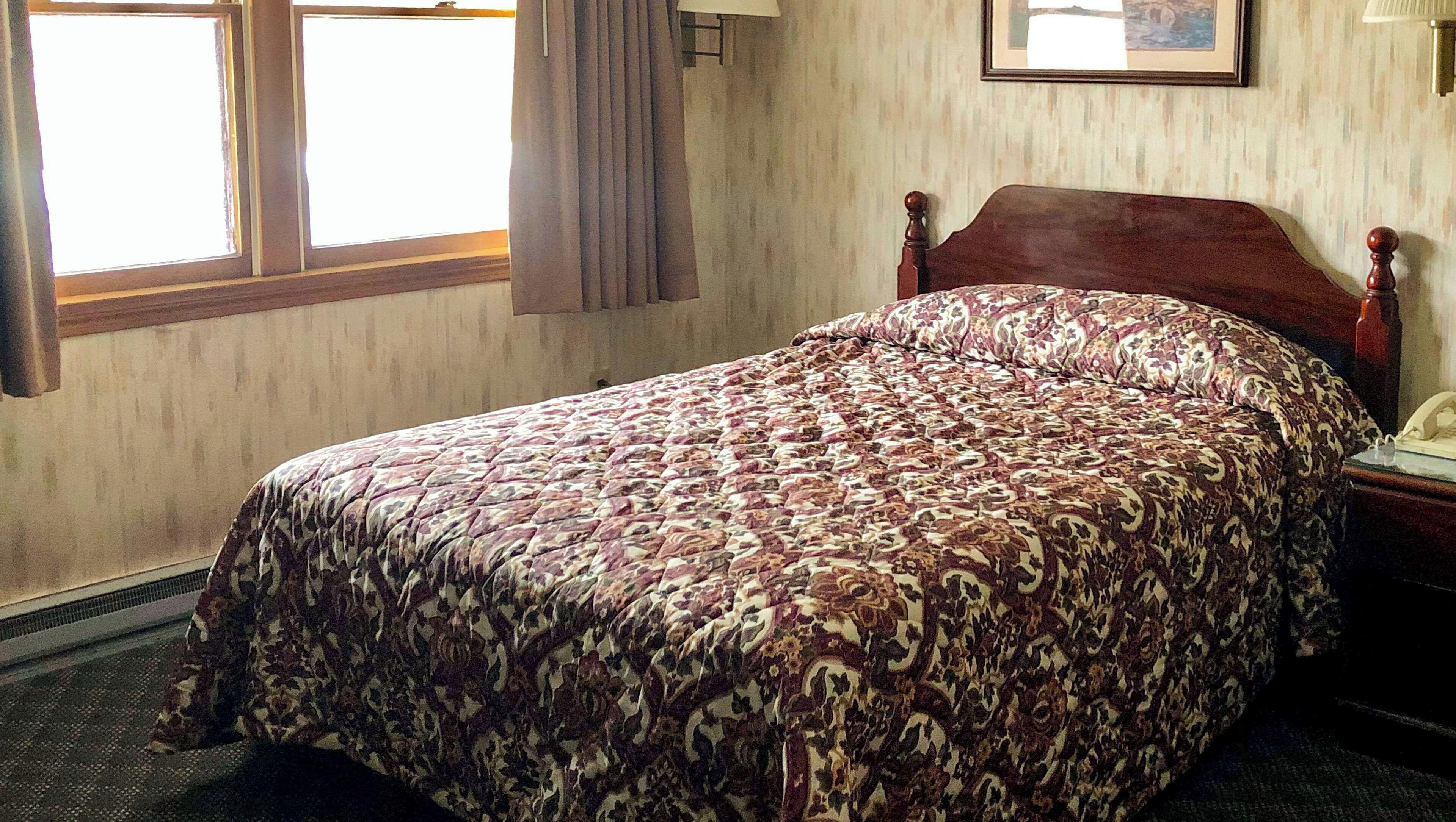 A hotel room with a bed, a window, a lamp, and a framed picture on the wall.