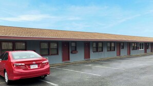 A motel with a row of rooms, a parking lot, and a red car parked in front.