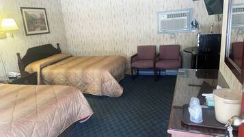 Habitación de hotel con dos camas, un escritorio con espejo, una silla, televisión y aire acondicionado.