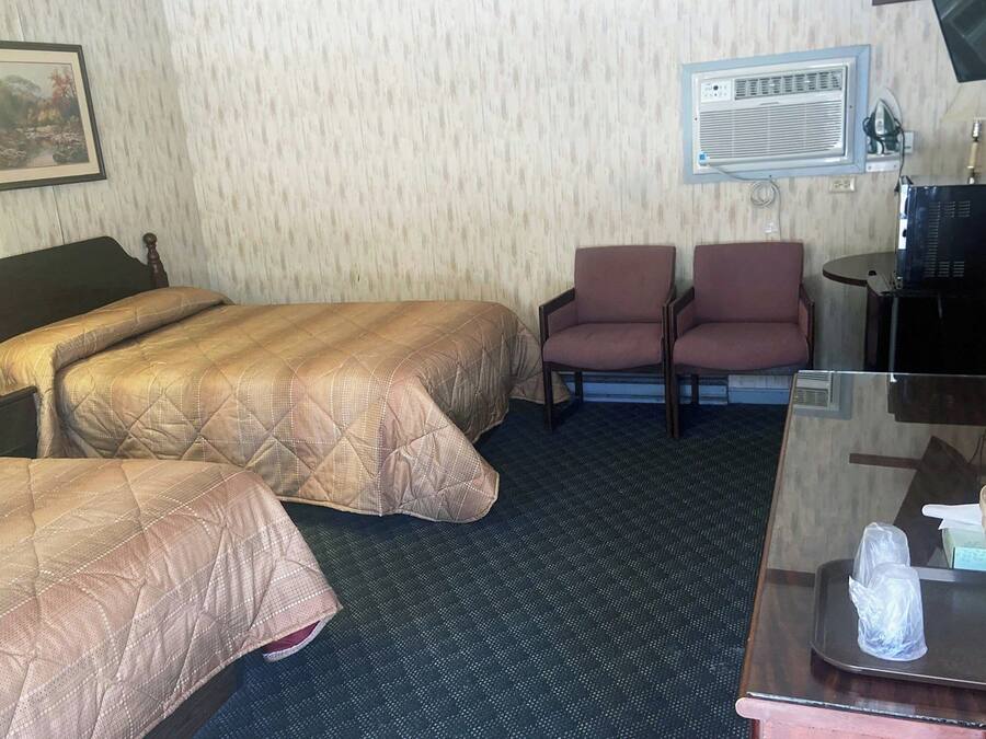 Habitación de hotel con dos camas, un escritorio con espejo, una silla, televisión y aire acondicionado.