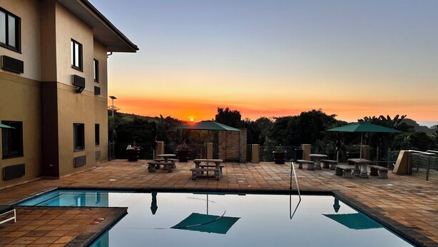 A swimming pool with a sunset view, outdoor seating, and a building with multiple windows.