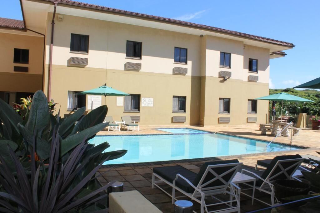 A hotel with a swimming pool, sun loungers, and umbrellas.